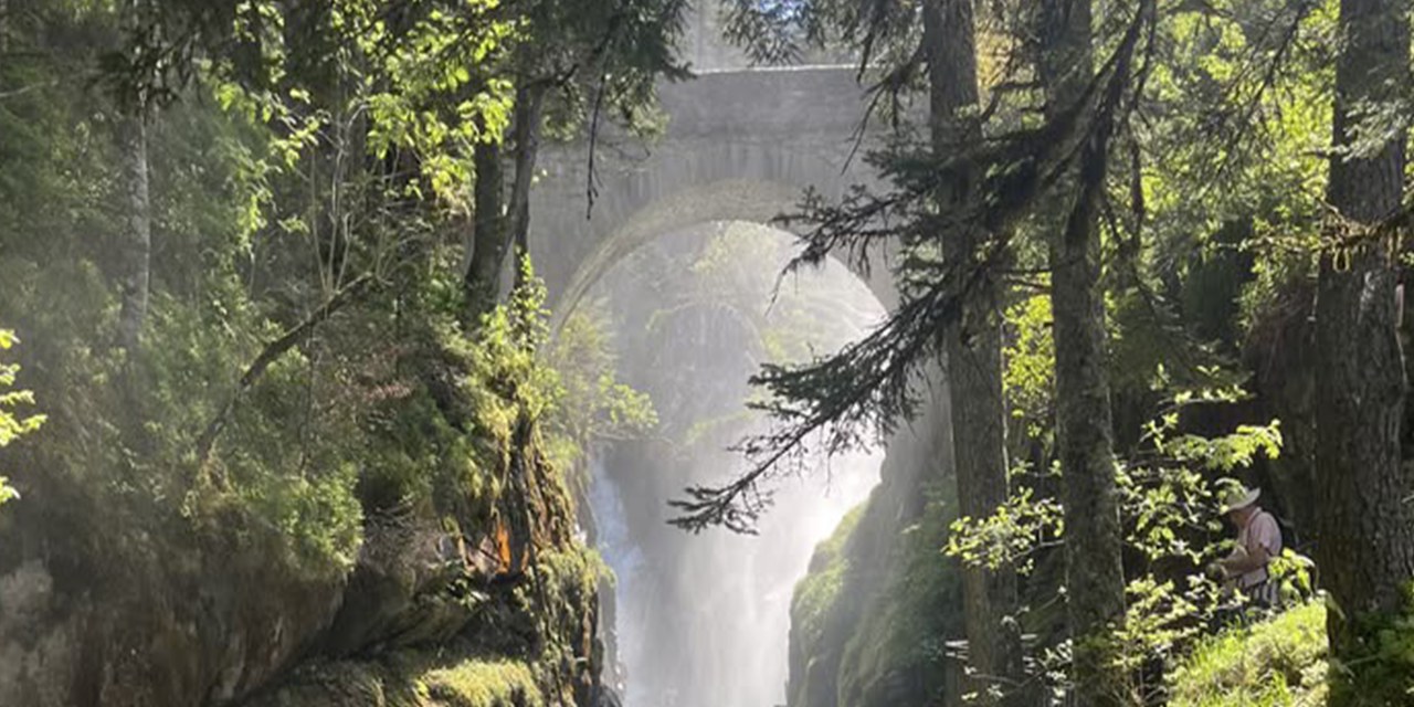 Un vieux pont de pierre enjambe une gorge boisée où tombe une cascade