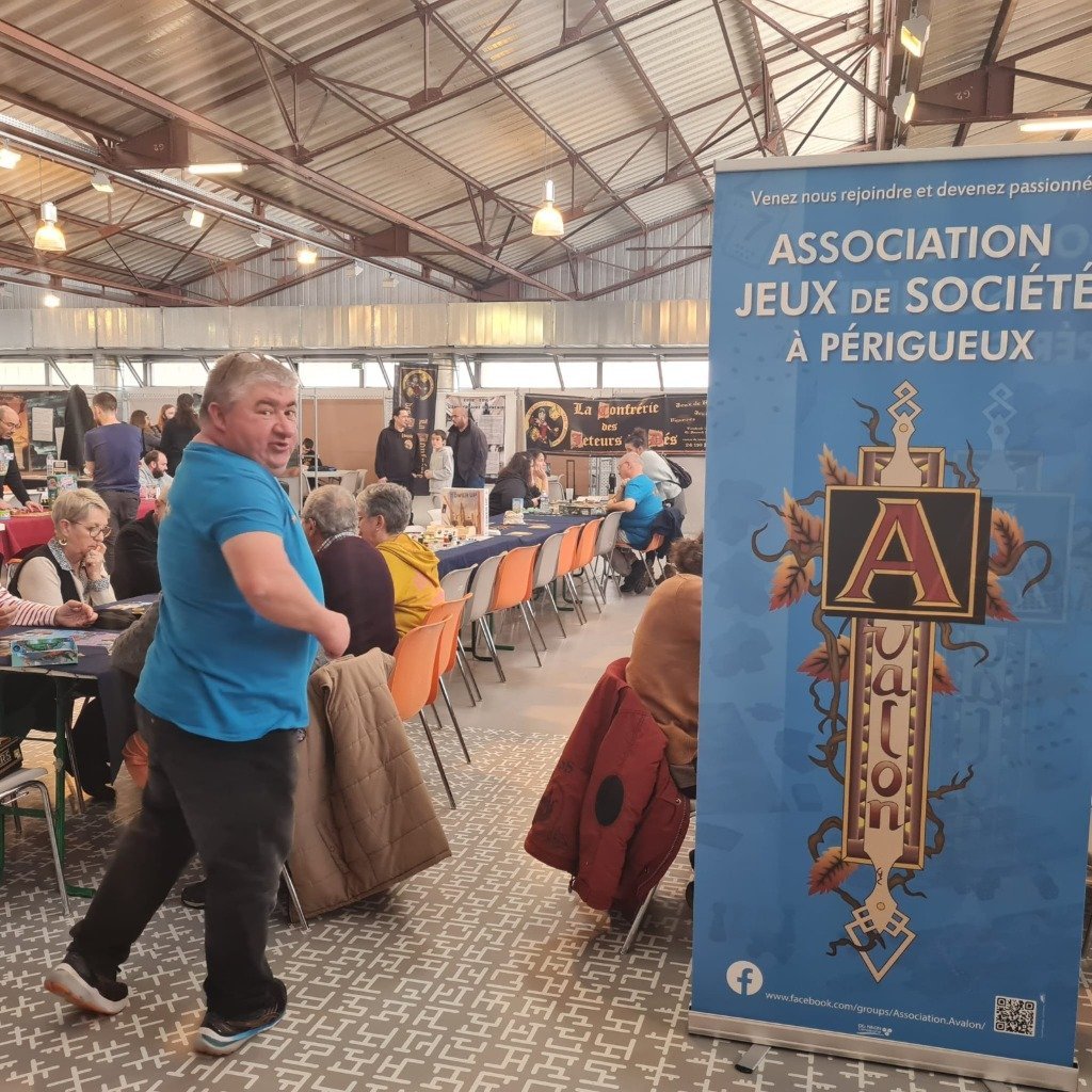 Francis avec le t-shirt bleu d'Avalon devant le stand et l'oriflamme de l'association